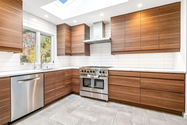 kitchen with wall chimney range hood, sink, a skylight, appliances with stainless steel finishes, and tasteful backsplash