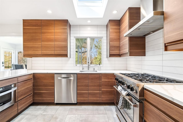 kitchen with a wealth of natural light, wall chimney range hood, appliances with stainless steel finishes, and a skylight