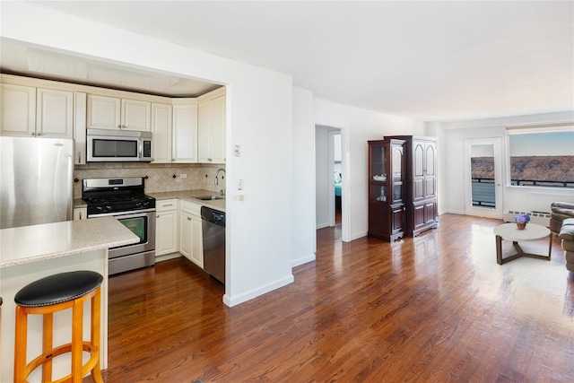 kitchen featuring decorative backsplash, appliances with stainless steel finishes, dark hardwood / wood-style flooring, a kitchen bar, and sink