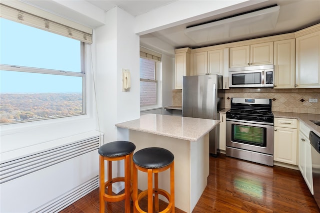 kitchen with stainless steel appliances, tasteful backsplash, light stone counters, cream cabinets, and a breakfast bar