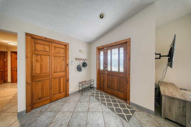 entrance foyer with light tile patterned floors, a textured ceiling, and vaulted ceiling