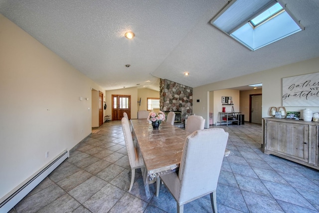 dining space featuring baseboard heating, a stone fireplace, vaulted ceiling with skylight, and a textured ceiling