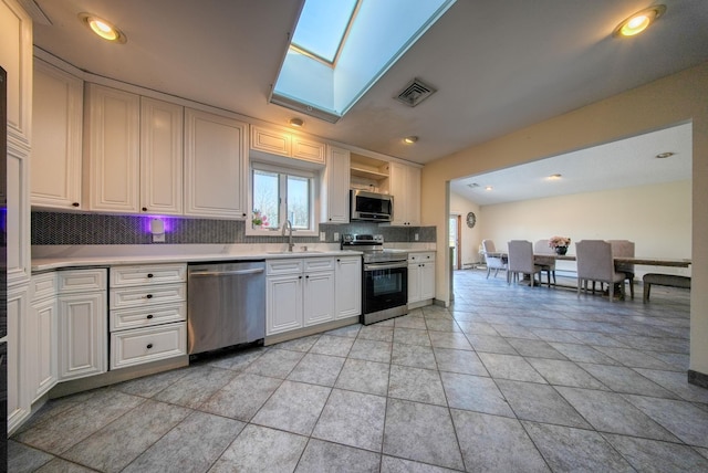 kitchen with tasteful backsplash, white cabinetry, appliances with stainless steel finishes, and a skylight