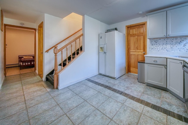 kitchen featuring sink, baseboard heating, white refrigerator with ice dispenser, backsplash, and light tile patterned flooring