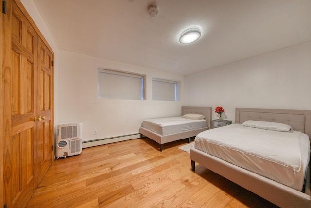 bedroom with a closet, light wood-type flooring, a wall unit AC, and a baseboard radiator