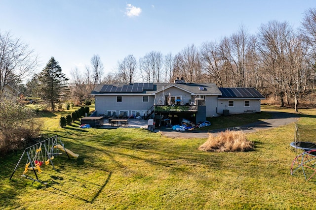 back of house with solar panels, a wooden deck, a trampoline, a yard, and a playground