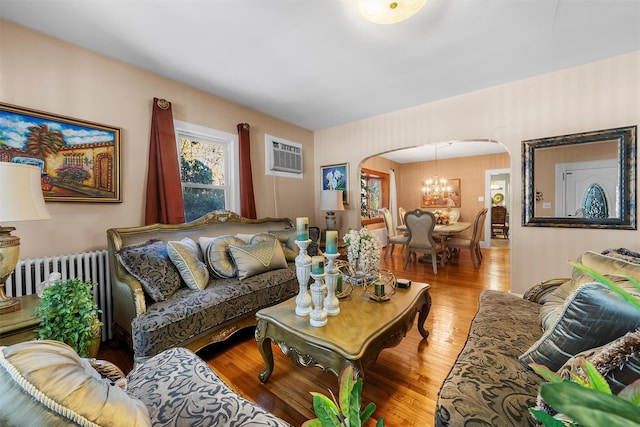 living room featuring a wall unit AC, radiator heating unit, a notable chandelier, and light wood-type flooring