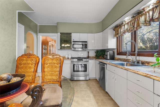 kitchen featuring sink, light tile patterned floors, appliances with stainless steel finishes, white cabinets, and decorative backsplash