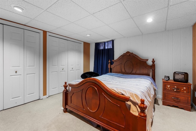 bedroom featuring multiple closets, light colored carpet, and a drop ceiling