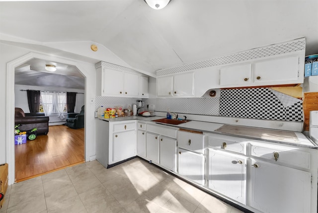 kitchen featuring lofted ceiling, sink, light tile patterned floors, white cabinetry, and backsplash