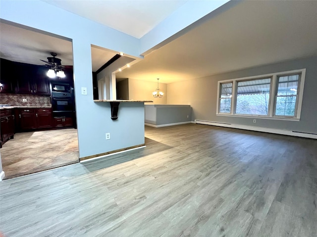 unfurnished living room featuring baseboard heating, ceiling fan with notable chandelier, and light wood-type flooring