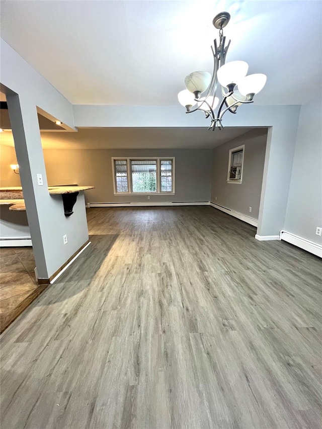 unfurnished living room featuring hardwood / wood-style flooring, baseboard heating, and an inviting chandelier