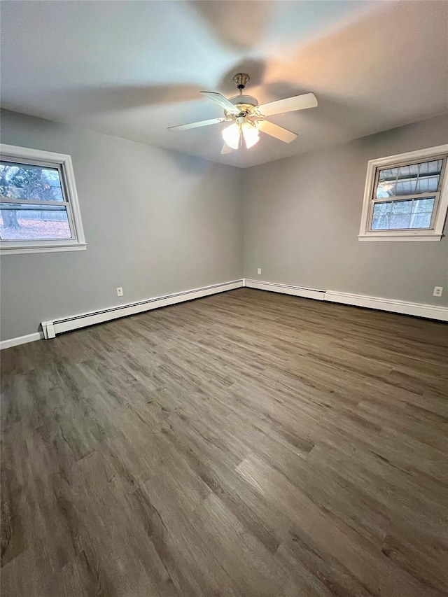 unfurnished room featuring dark wood-type flooring, baseboard heating, and a healthy amount of sunlight