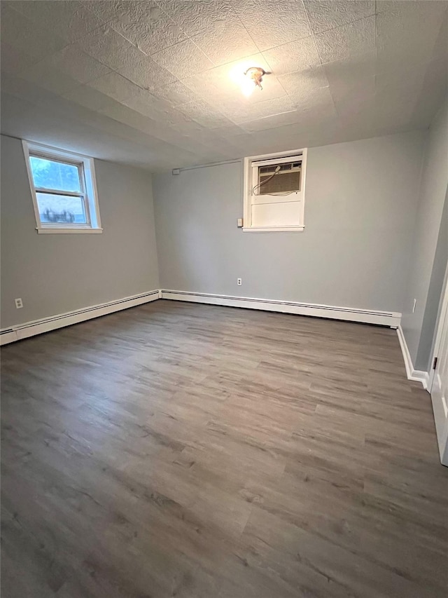 basement with a wall unit AC, hardwood / wood-style floors, a textured ceiling, and baseboard heating