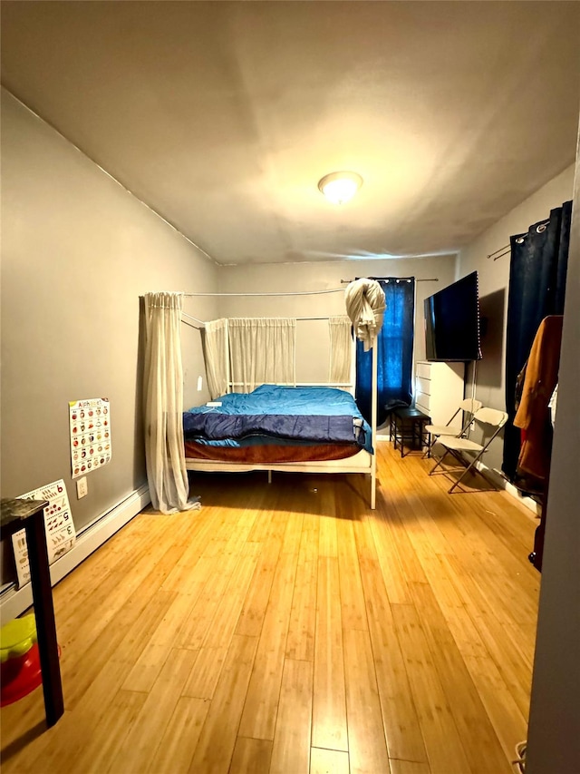 unfurnished bedroom featuring hardwood / wood-style floors and a baseboard heating unit