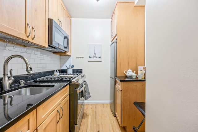 kitchen featuring sink, dark stone countertops, appliances with stainless steel finishes, tasteful backsplash, and light hardwood / wood-style floors