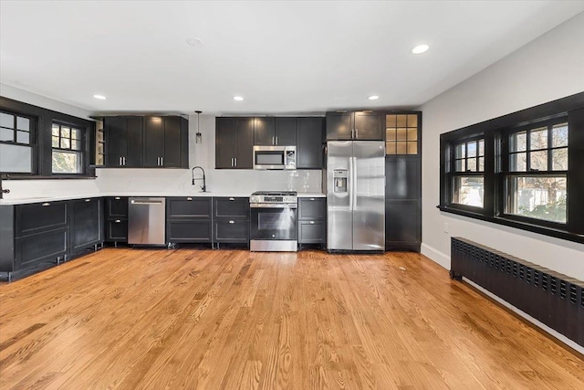 kitchen featuring light wood-type flooring, sink, radiator heating unit, and appliances with stainless steel finishes