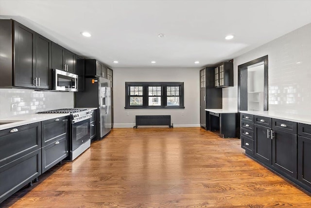 kitchen featuring radiator, sink, decorative backsplash, stainless steel appliances, and light wood-type flooring