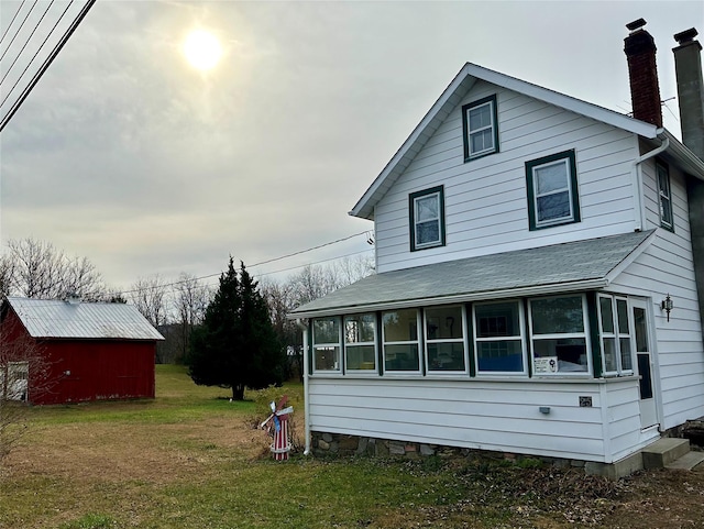 back of house with a lawn, a sunroom, and an outdoor structure