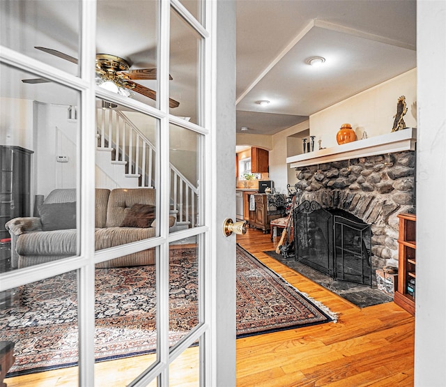 living room featuring hardwood / wood-style floors, a stone fireplace, and ceiling fan