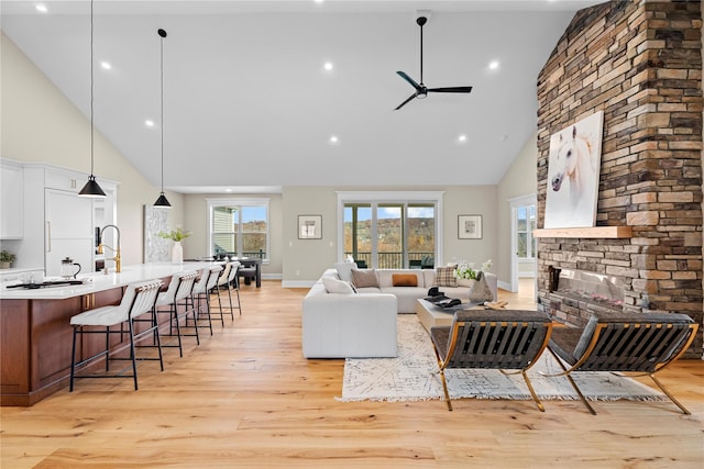 living room with ceiling fan, a stone fireplace, high vaulted ceiling, and light hardwood / wood-style flooring