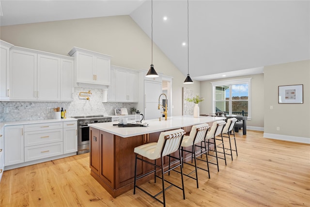 kitchen with white cabinets, high vaulted ceiling, high end stainless steel range oven, and a kitchen island with sink