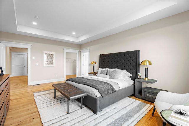 bedroom featuring a raised ceiling, a spacious closet, a closet, and light hardwood / wood-style floors