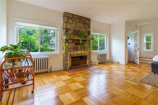 living room with a stone fireplace, radiator heating unit, and light parquet floors