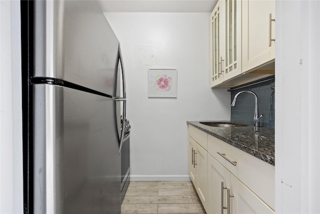 kitchen with stainless steel fridge, tasteful backsplash, sink, light hardwood / wood-style flooring, and dark stone countertops