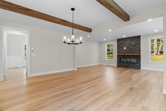 unfurnished living room featuring beam ceiling, a fireplace, an inviting chandelier, and light wood-type flooring