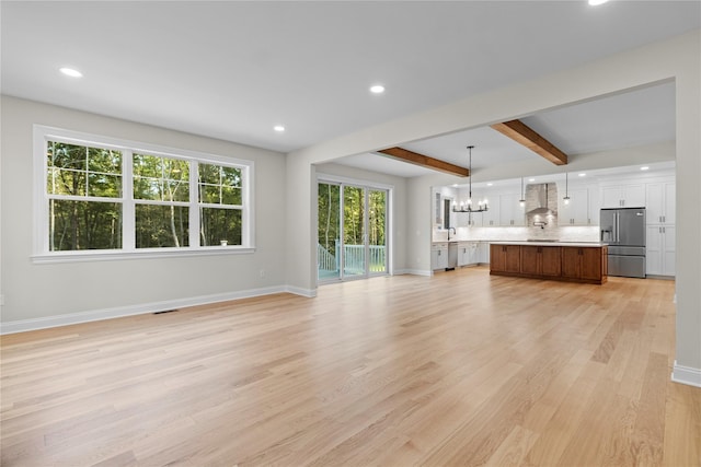 unfurnished living room featuring beamed ceiling, light hardwood / wood-style floors, and an inviting chandelier