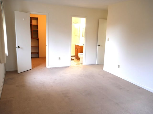 unfurnished bedroom with ensuite bathroom, light colored carpet, a walk in closet, and a closet