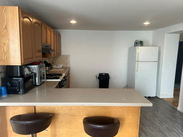 kitchen with a kitchen bar, stainless steel range with gas cooktop, white fridge, dark hardwood / wood-style flooring, and kitchen peninsula