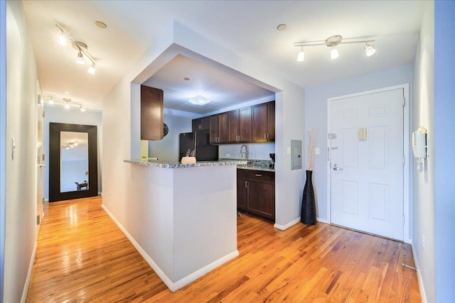 kitchen featuring black fridge, sink, light hardwood / wood-style flooring, dark brown cabinetry, and light stone counters