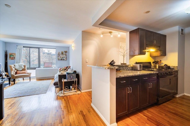 kitchen with light wood-type flooring, black gas range oven, light stone counters, and dark brown cabinetry