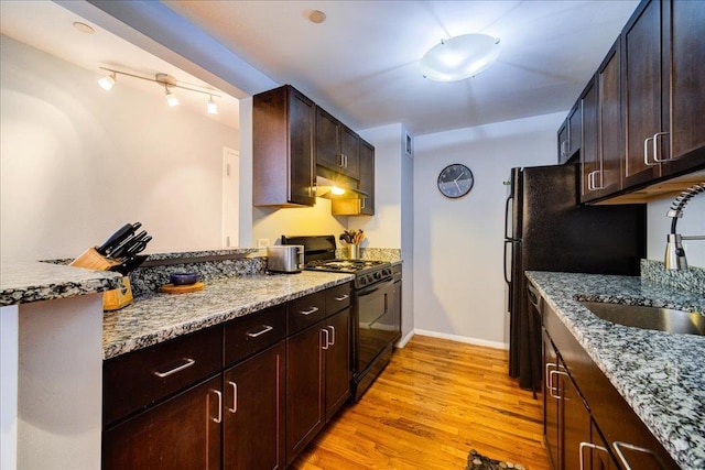 kitchen featuring light wood-type flooring, light stone countertops, black gas stove, and sink