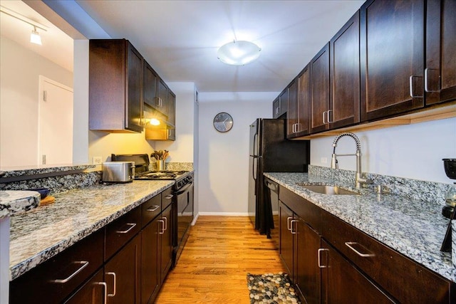 kitchen with black gas range, light stone countertops, light hardwood / wood-style flooring, and sink