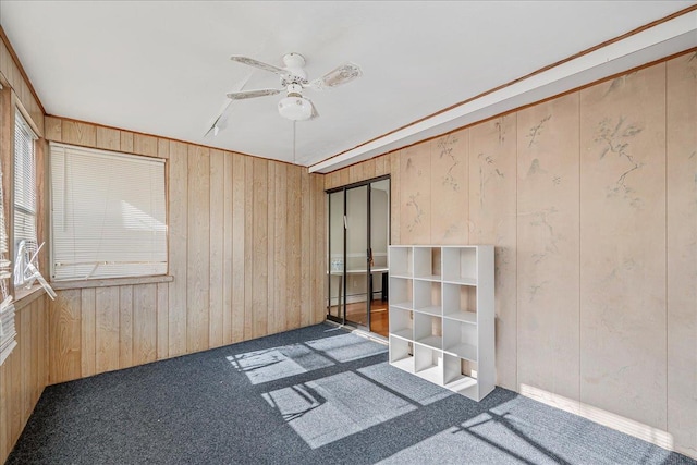 empty room with dark colored carpet, ceiling fan, and wooden walls