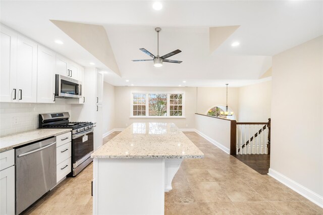 kitchen featuring a center island, lofted ceiling, appliances with stainless steel finishes, light stone counters, and white cabinetry