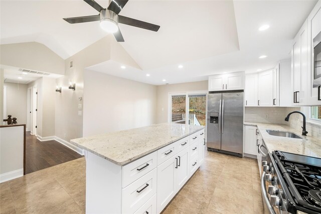 kitchen with a center island, vaulted ceiling, light stone countertops, white cabinetry, and stainless steel appliances