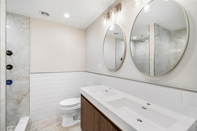 bathroom featuring vanity, toilet, tile walls, and a tile shower