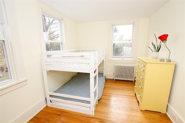 bedroom featuring radiator heating unit, light hardwood / wood-style flooring, and multiple windows