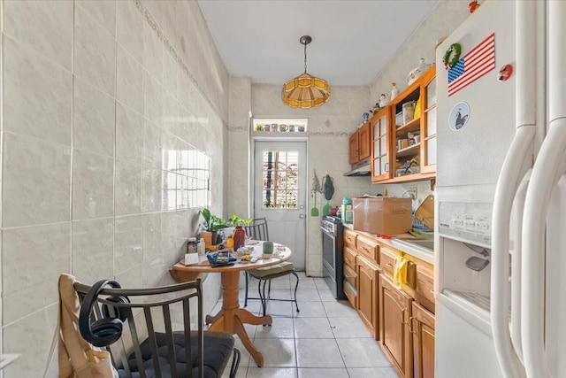 kitchen with white fridge with ice dispenser, tile walls, light tile patterned floors, stainless steel range, and decorative light fixtures