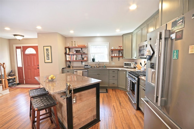 kitchen with light stone countertops, a breakfast bar, premium appliances, light hardwood / wood-style flooring, and a center island