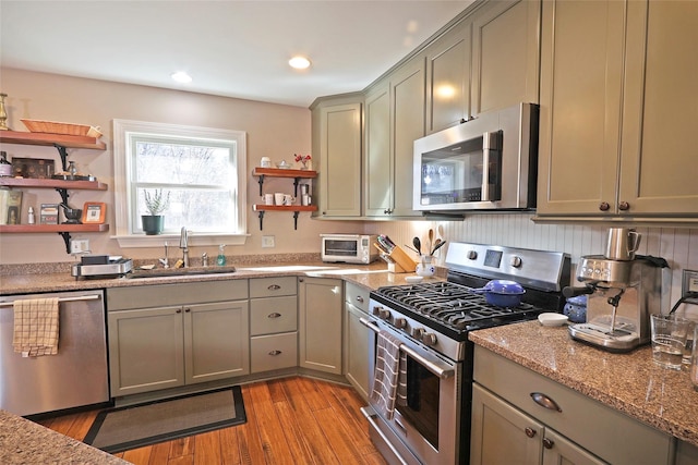 kitchen with sink, stainless steel appliances, light hardwood / wood-style flooring, and light stone counters