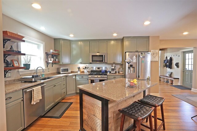 kitchen with light stone countertops, a kitchen bar, stainless steel appliances, and light hardwood / wood-style flooring