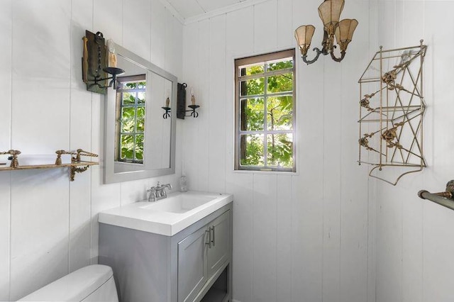 bathroom featuring vanity, toilet, crown molding, and wooden walls