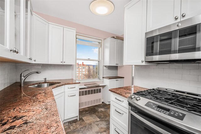 kitchen featuring radiator, sink, dark stone counters, white cabinets, and appliances with stainless steel finishes