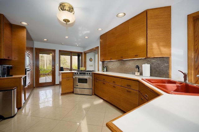 kitchen with sink, light tile patterned floors, kitchen peninsula, decorative backsplash, and stainless steel stove