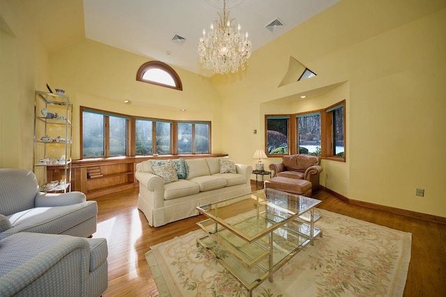 living room with a chandelier, light wood-type flooring, and a towering ceiling